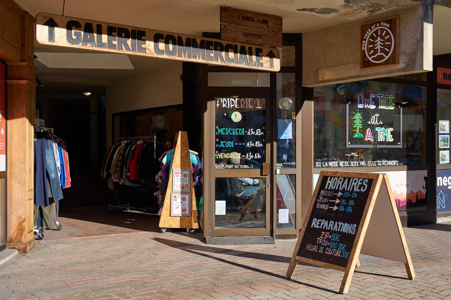 A sunny photo of the One Tree Shop Front with racks of repaired and second hand clothes outside.
