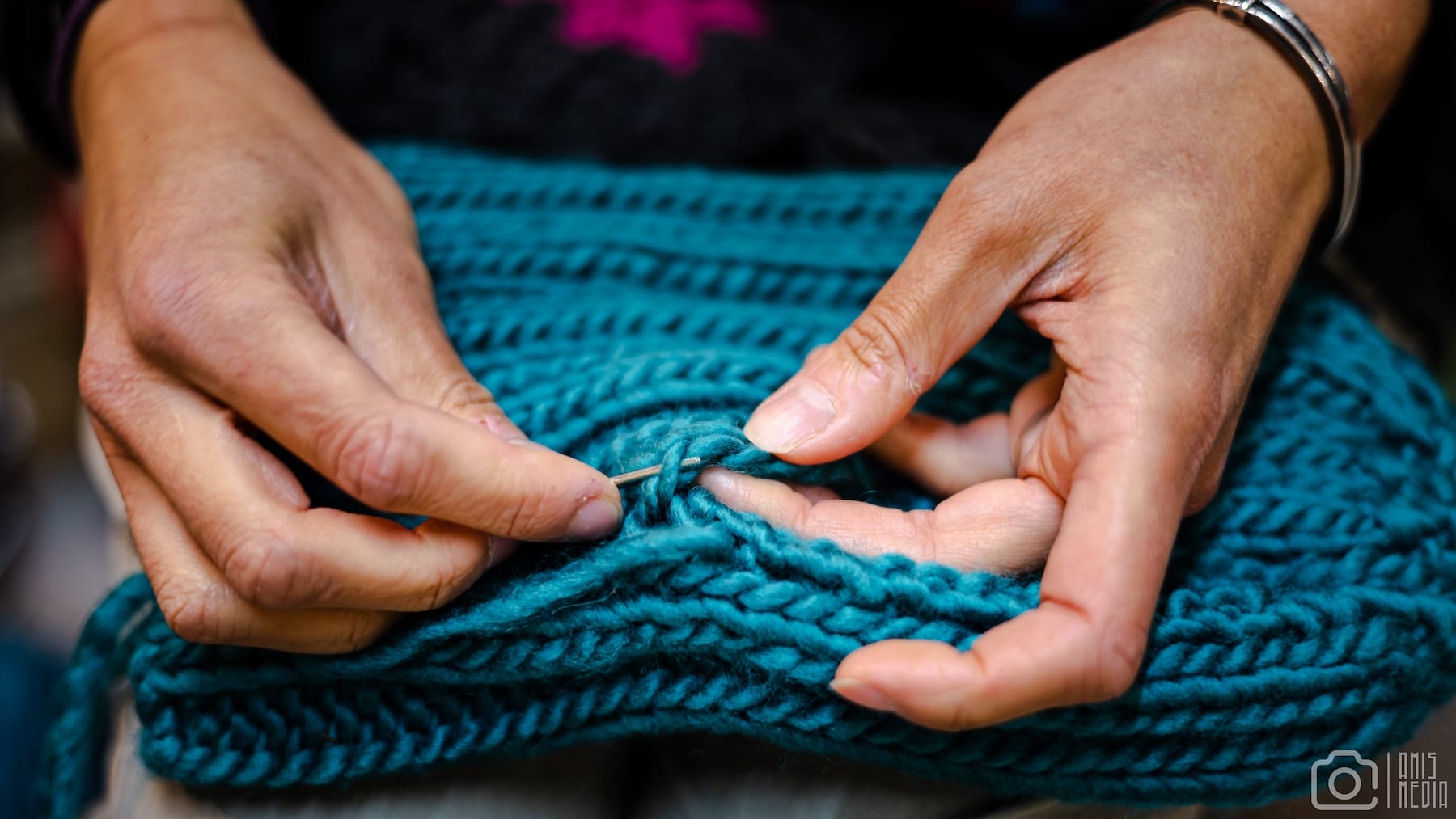 A pair of hands weaving woollen thread into a knitted scarf