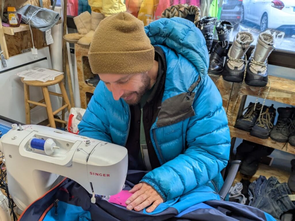 One Tree Founder Gav smiles as he works to patch a jacket with a sewing machine in the One Tree shop.
