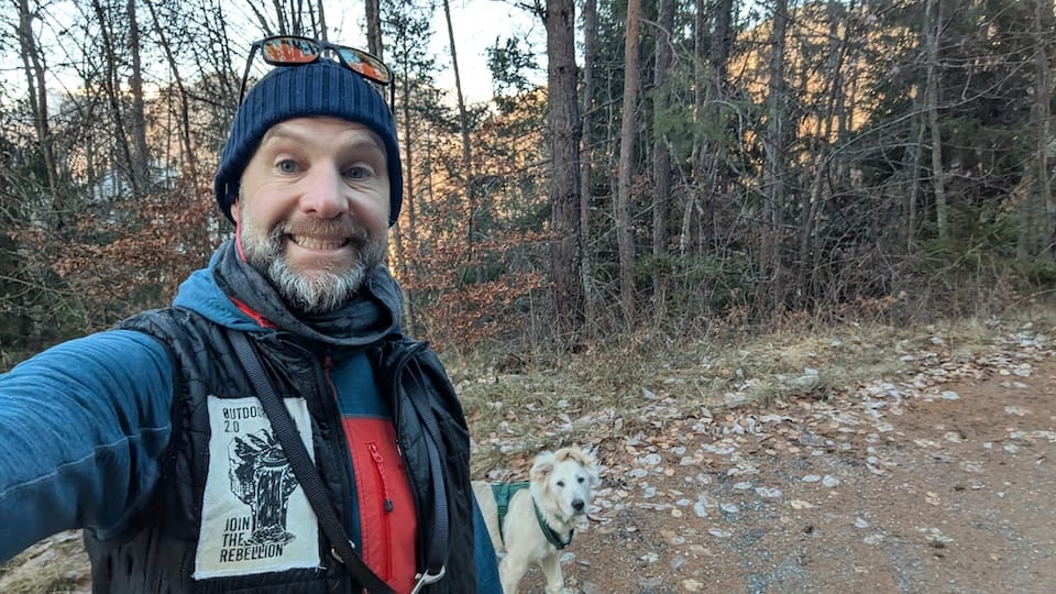 Andy smiling on a dog walk with his bemused dog watching on
