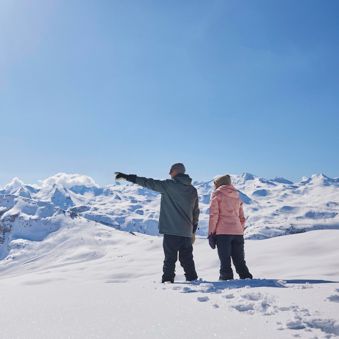 A male and female couple view the surrounding mounains from a snow field