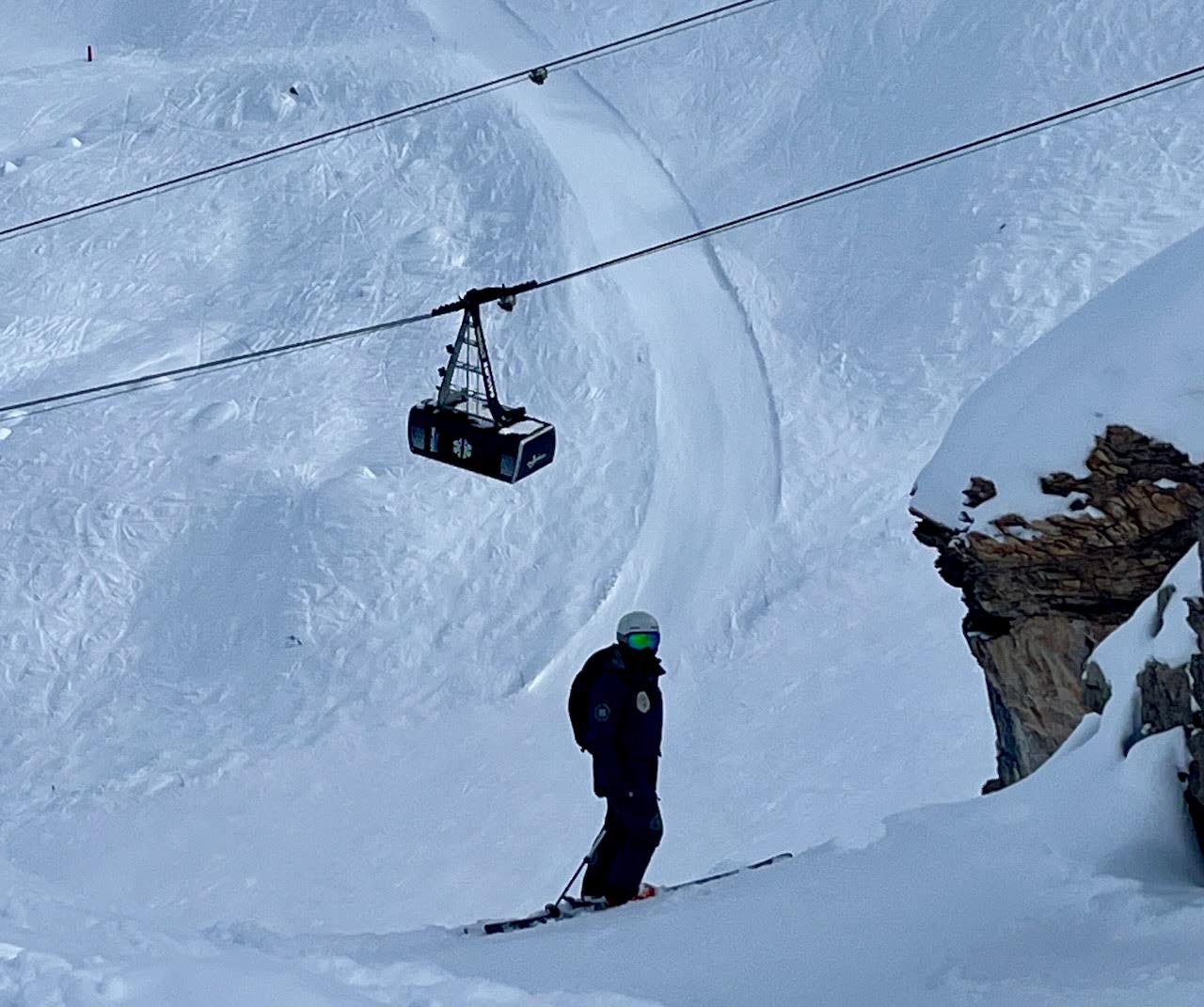 A skier in the offpiste with a large telecabine ski lift in the background
