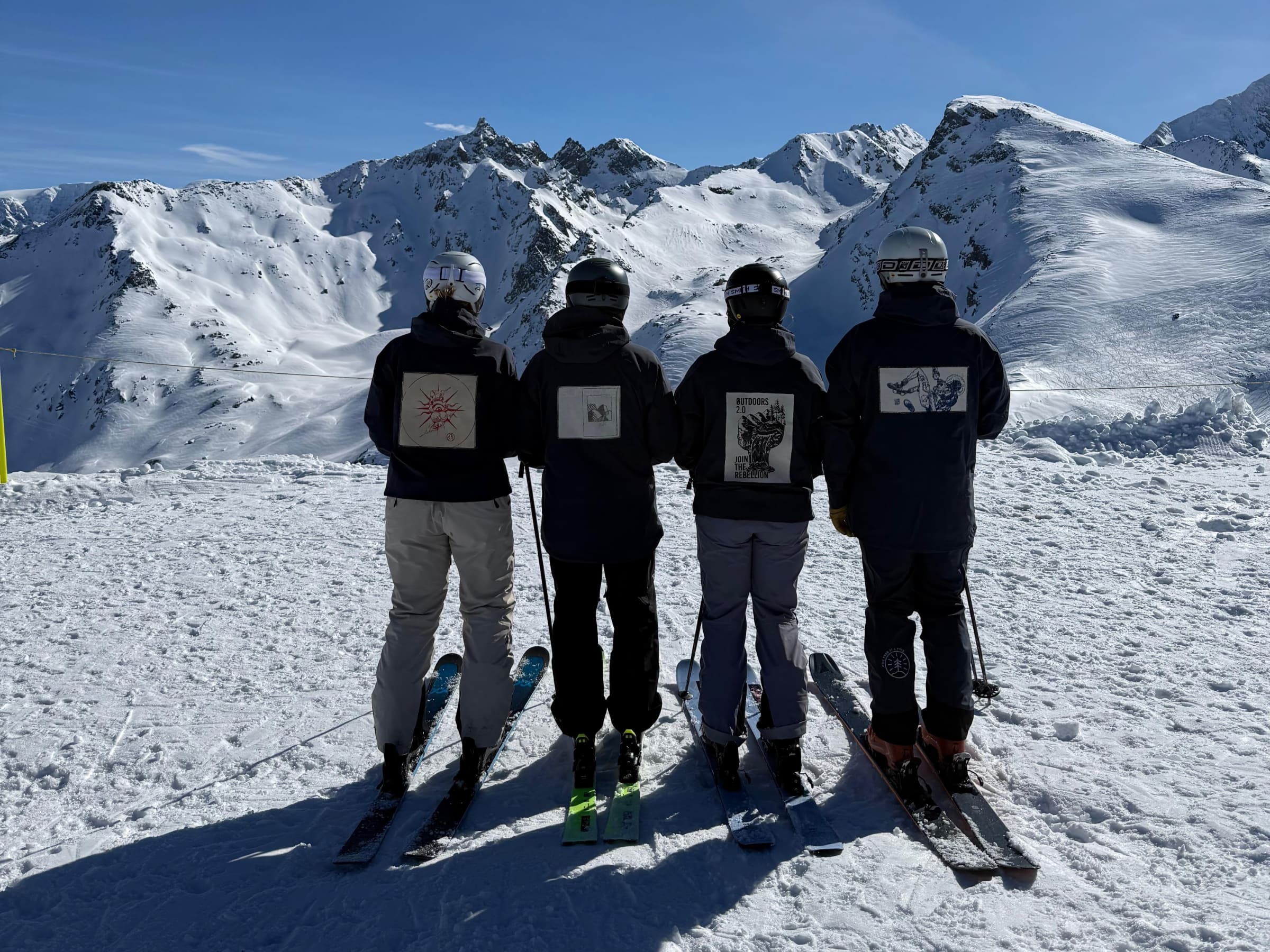 Four skiers in Made to be Worn jackets gave at the mountains, blue skies and sunshine